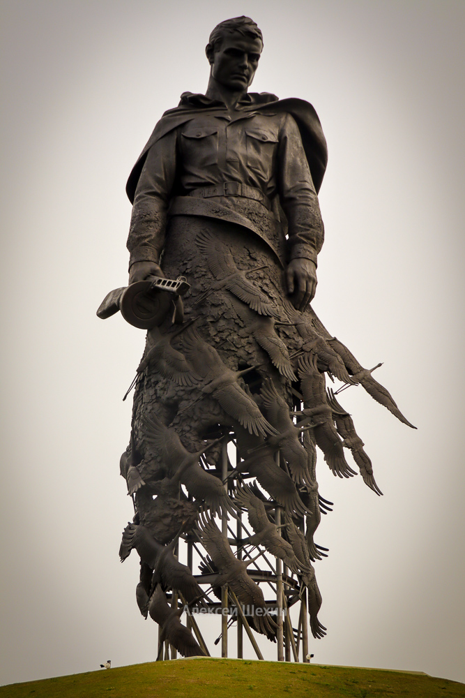 Скульптура солдата с развивающимся плащом с автоматом ППШ в руках, взгляд направлен вдаль, внизу журавли